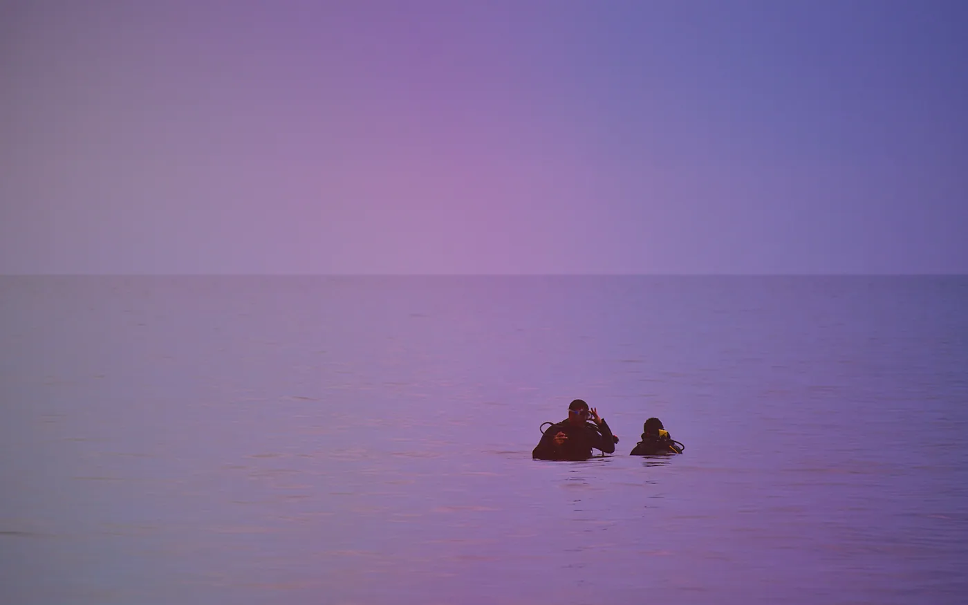 Two scuba divers at the surface on flat water in the last of the light