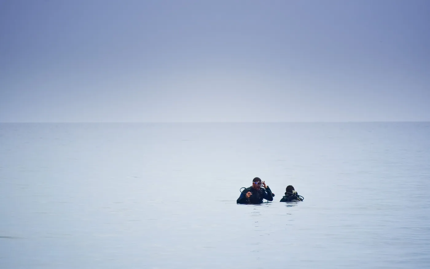 Two divers at the surface in a vast expanse of flat water