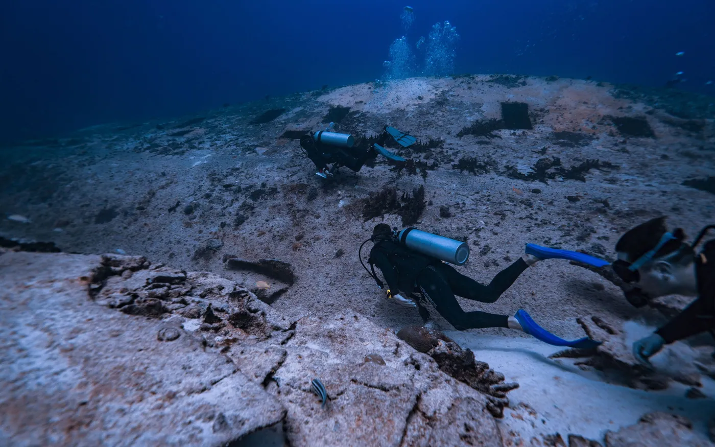 Two scuba divers swimming just clear of a rubble bottom without stirring it