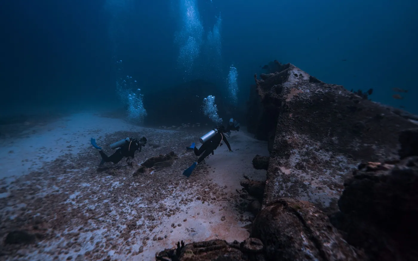 Two scuba divers over a dim bottom with columns of bubbles rising