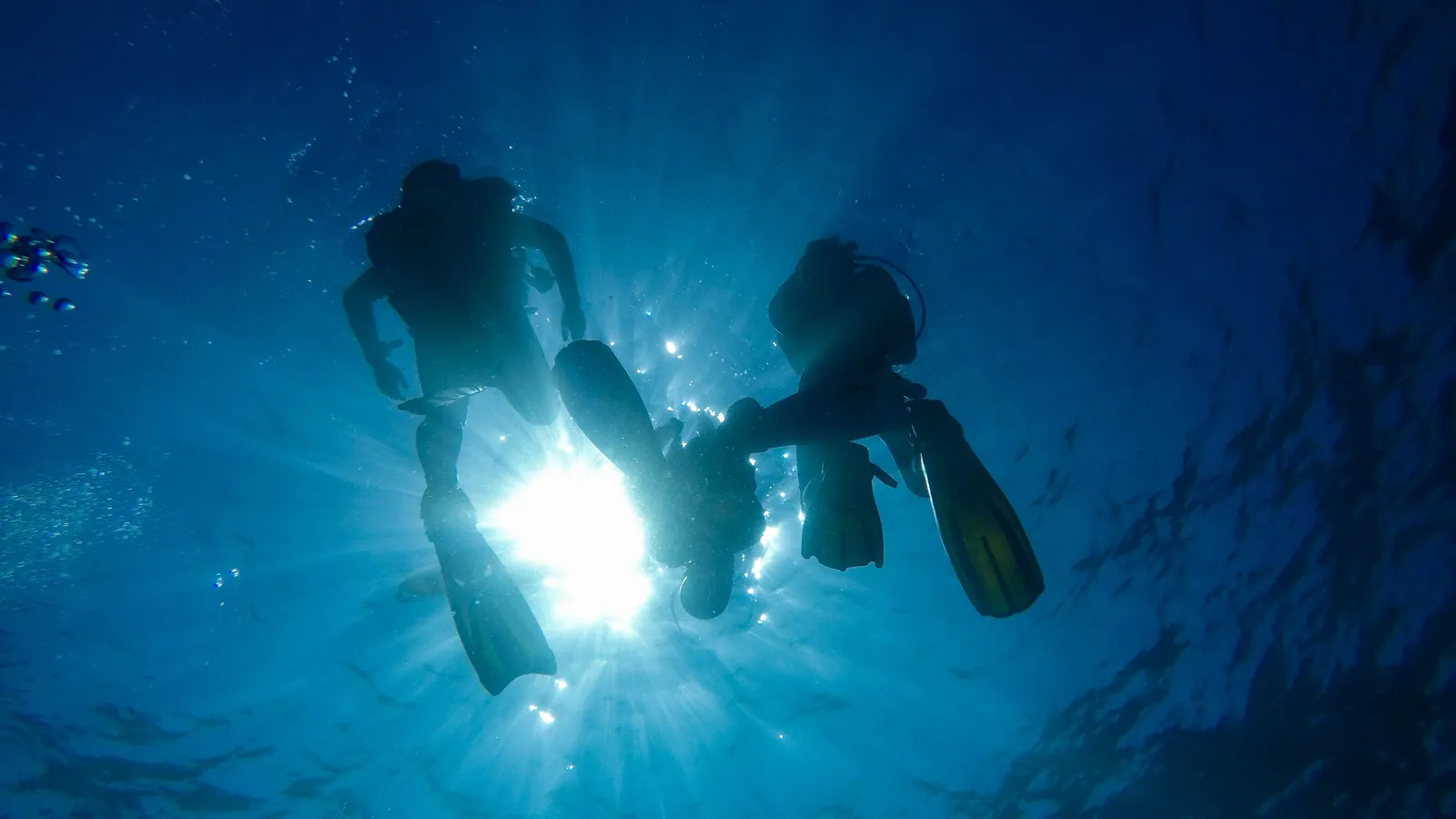 Two scuba divers seen from below against the sun, cylinders and fins silhouetted