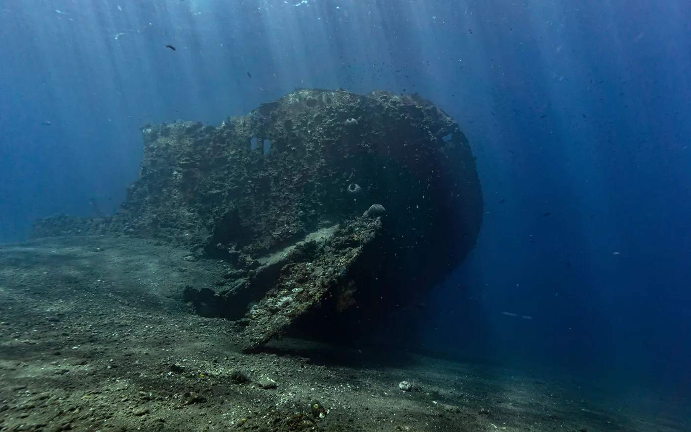 The hull of a shipwreck resting on the seabed in dark, low-visibility water