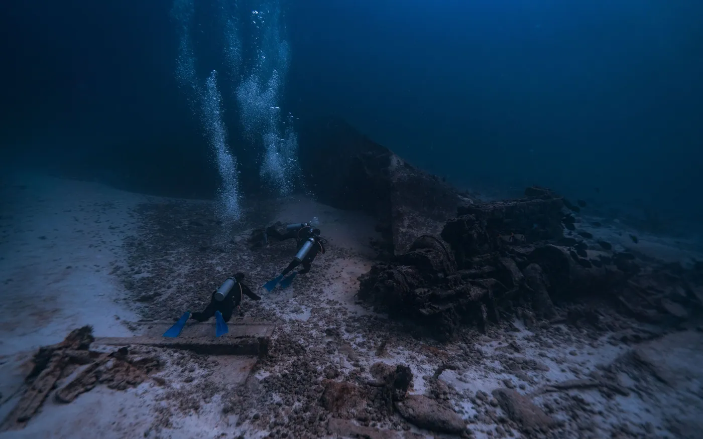 A diver above a wreck on a dark seabed